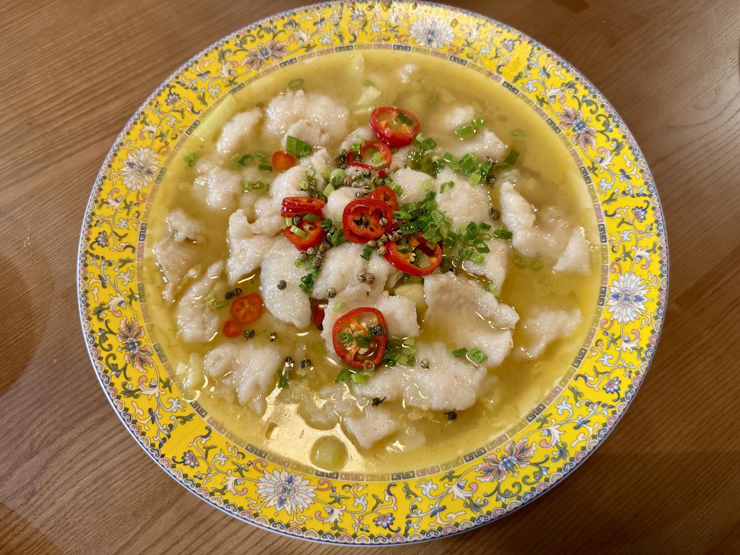 Sichuan-style fish fillet soup in yellow floral-patterned bowl with chili garnish at SoHo Asian Fusion, a Asian fusion restaurant in Austin