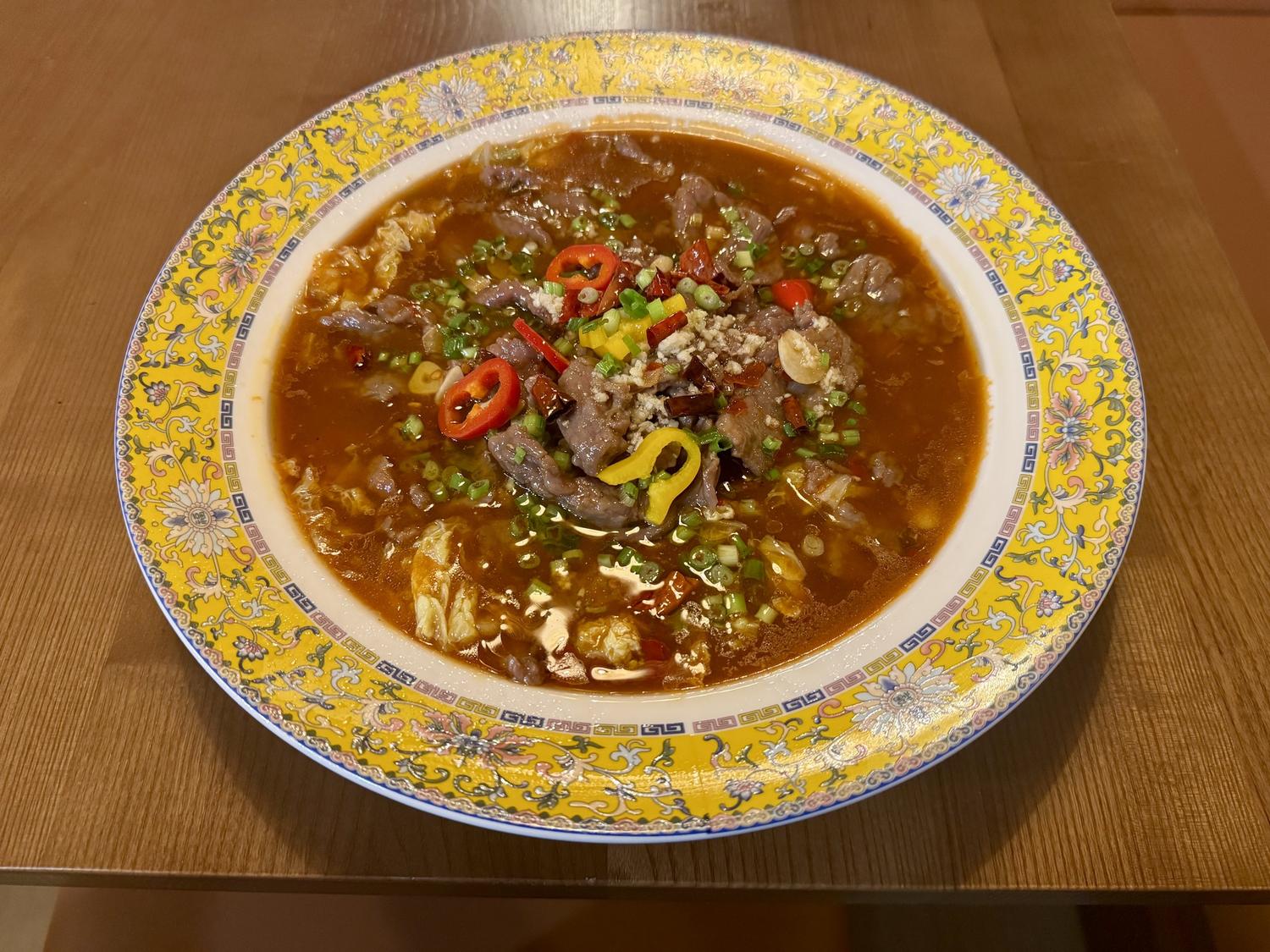 Spicy beef soup in ornate yellow bowl with red chili garnish at SoHo Asian Fusion, a Asian fusion restaurant in Austin