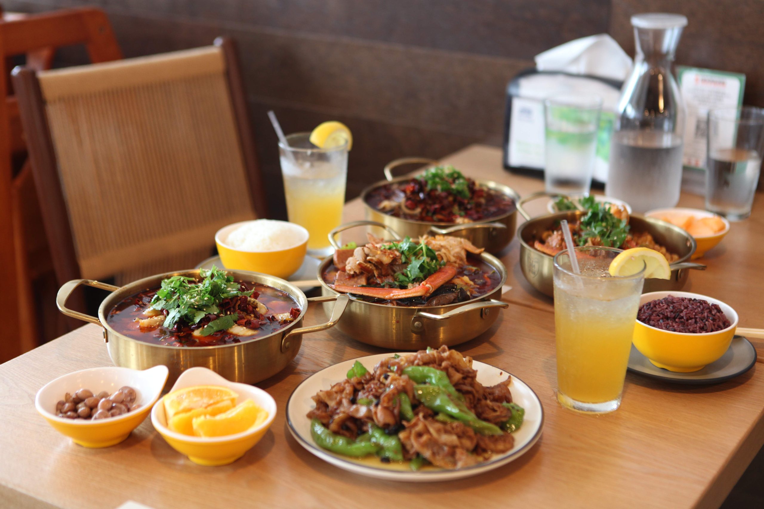 Chinese dry pot dishes with stir-fried beef, rice, fruit sides, and lemon drinks served family-style on a restaurant table