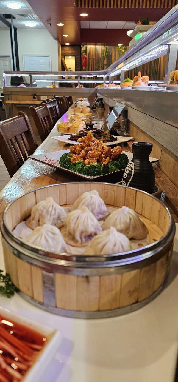 Soup dumplings in bamboo steamer with side stir fry dishes at Spin & Savor, a Conveyor Belt Sushi Restaurant in Rochester