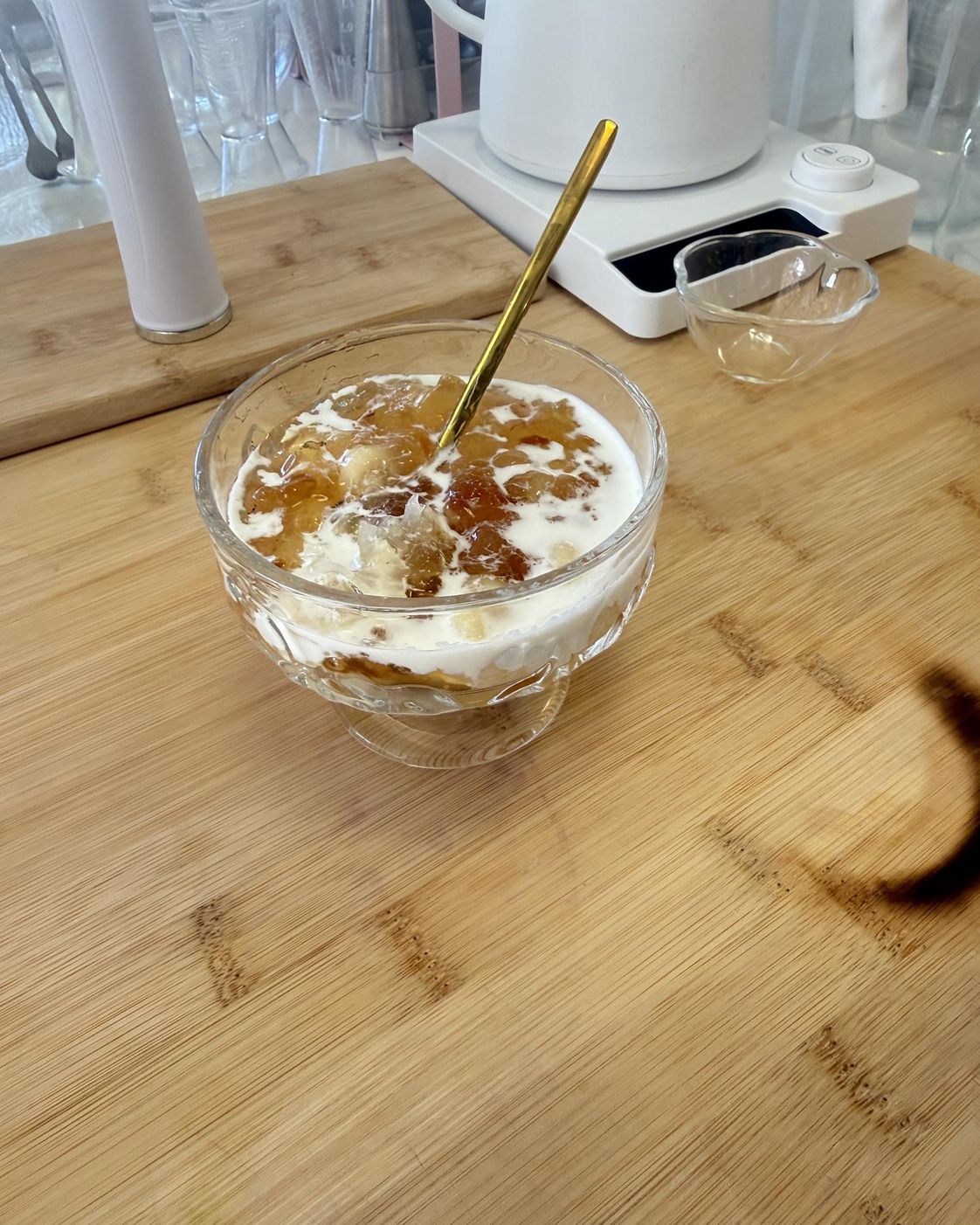 Glass bowl of peach gum dessert with milk and a gold spoon on a bamboo board