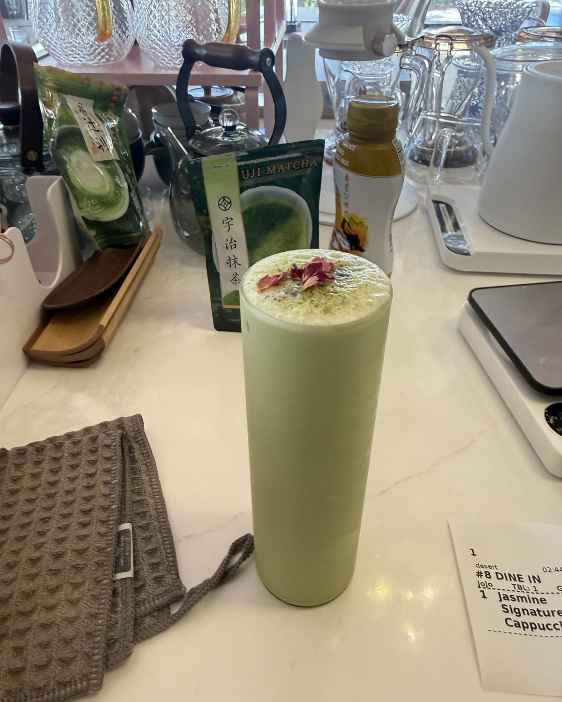 Iced matcha latte in a tall glass with pink petals and tea packaging