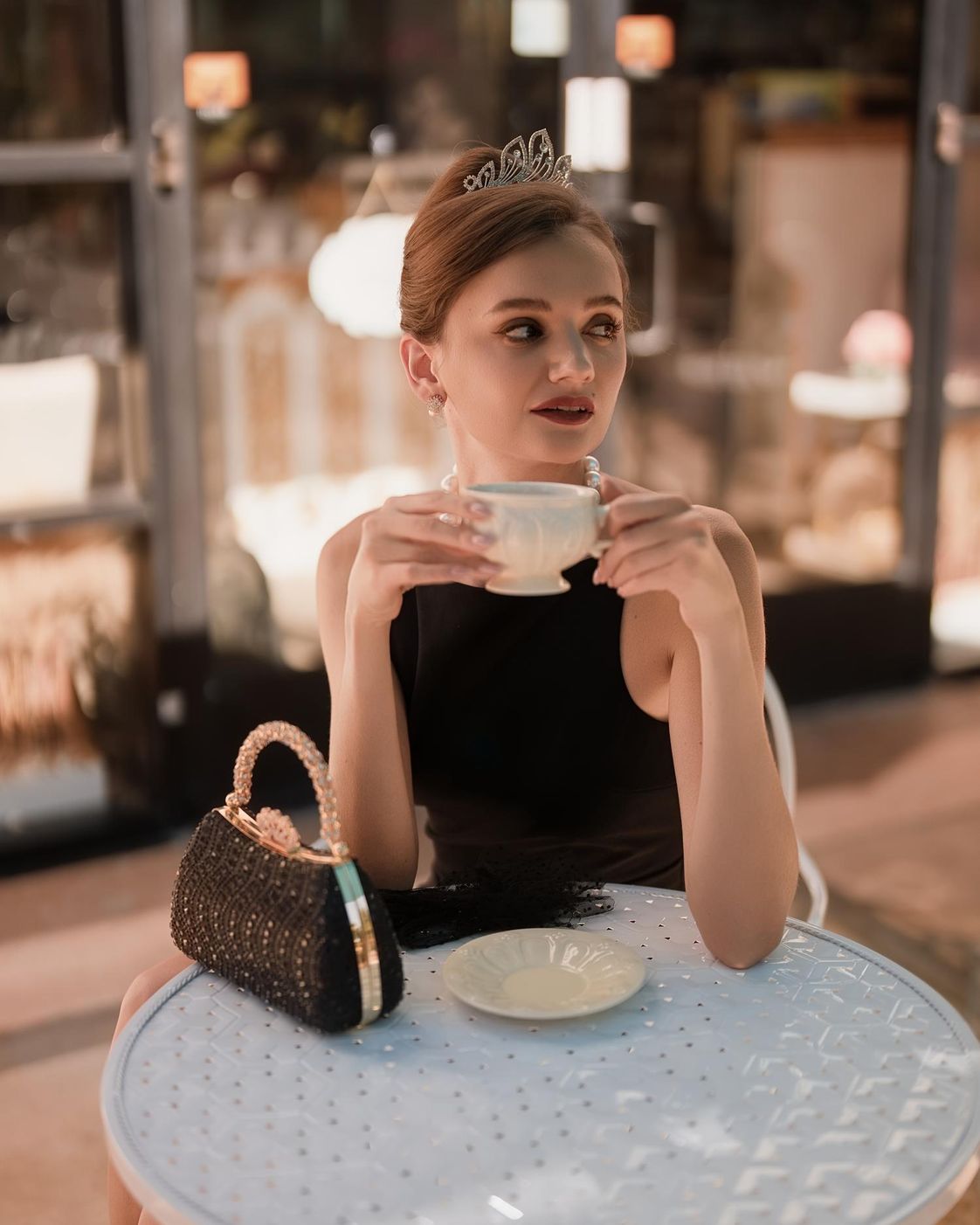 Woman in a black dress and tiara drinking tea at a cafe table