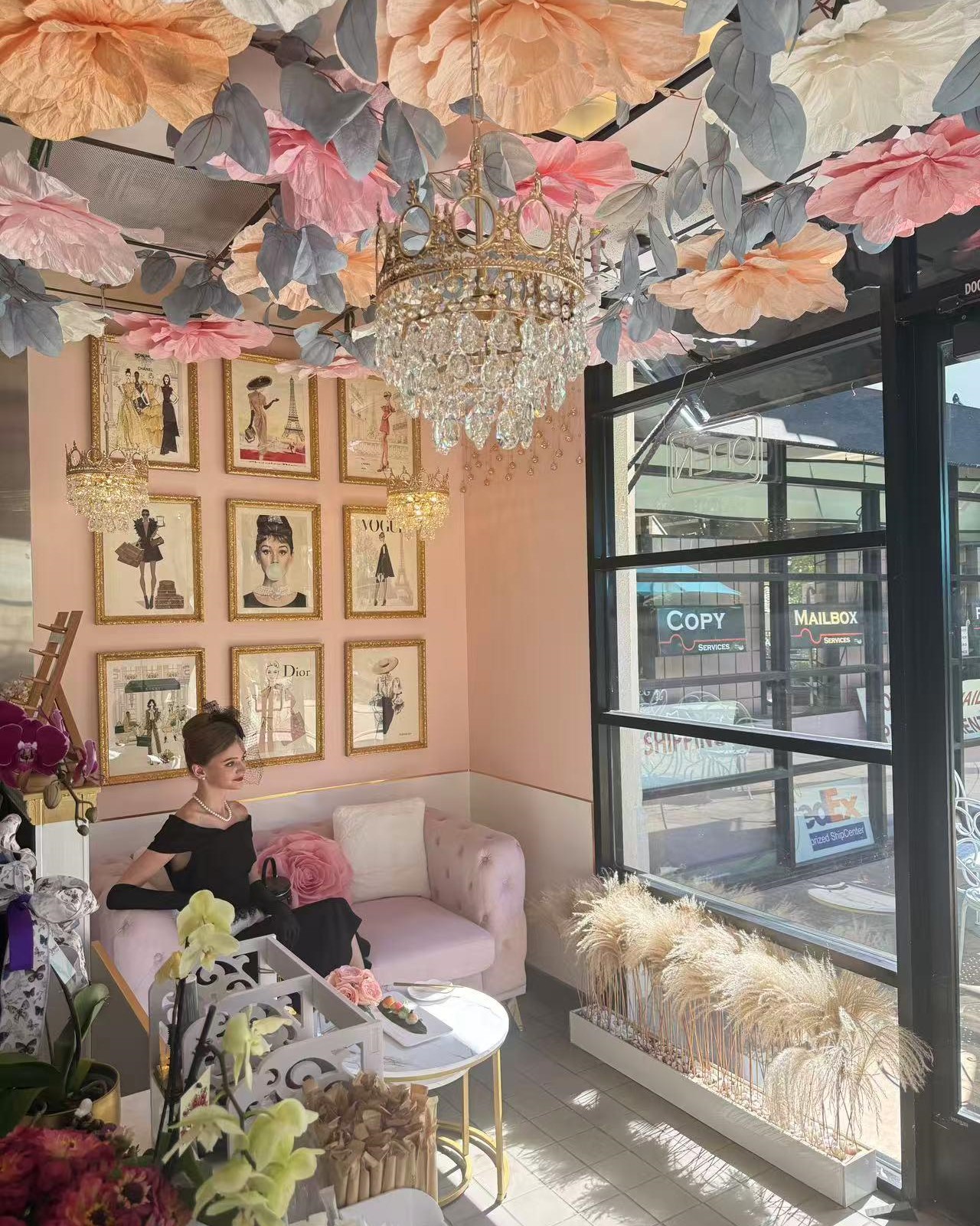 Stylish pink‑toned boutique cafe with hanging paper flowers, crystal chandeliers and vintage wall art