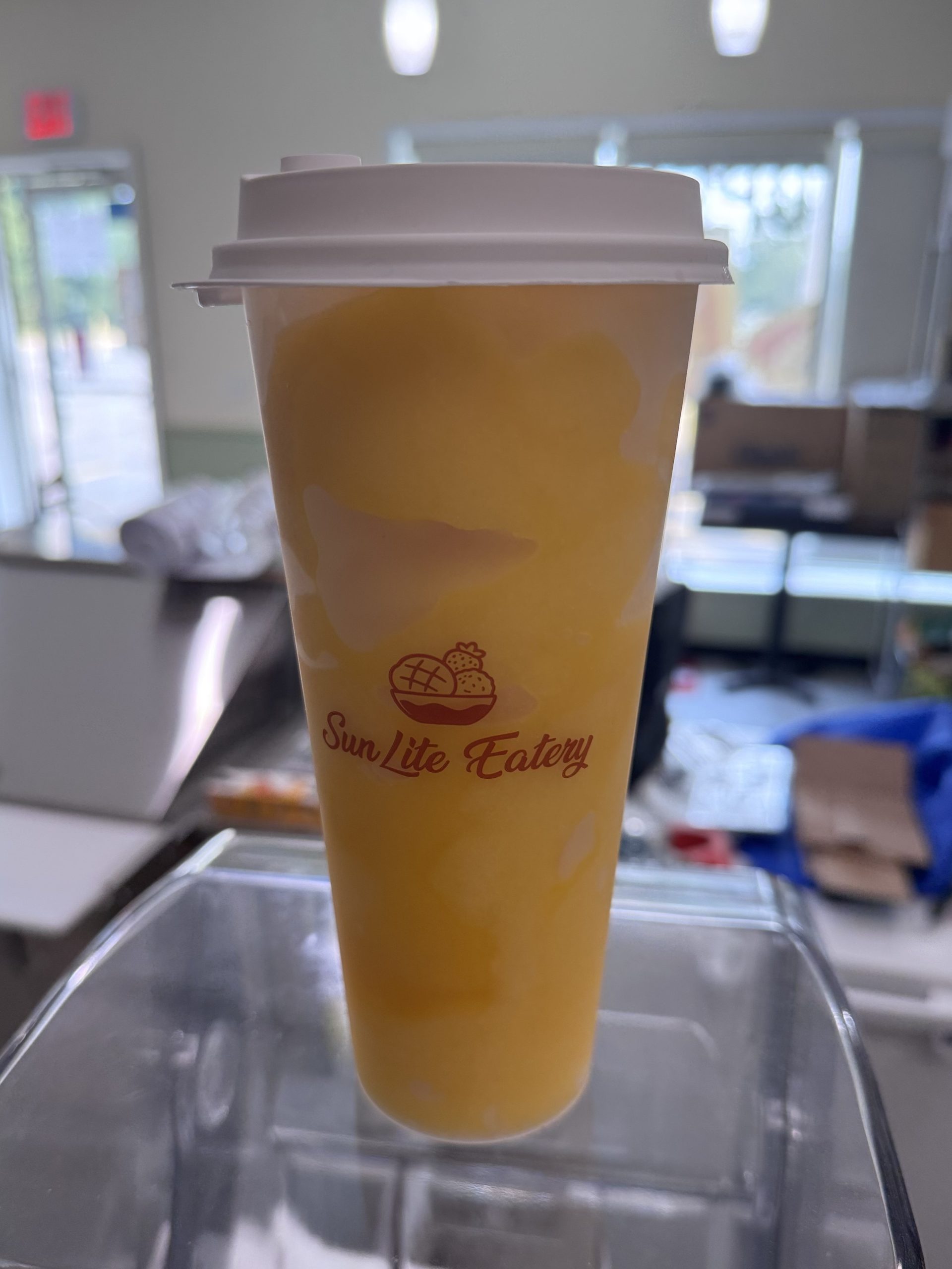 Creamy yellow tropical fruit smoothie in branded plastic cup at SunLite Eatery，an Asian Fusion Restaurant in Rochester