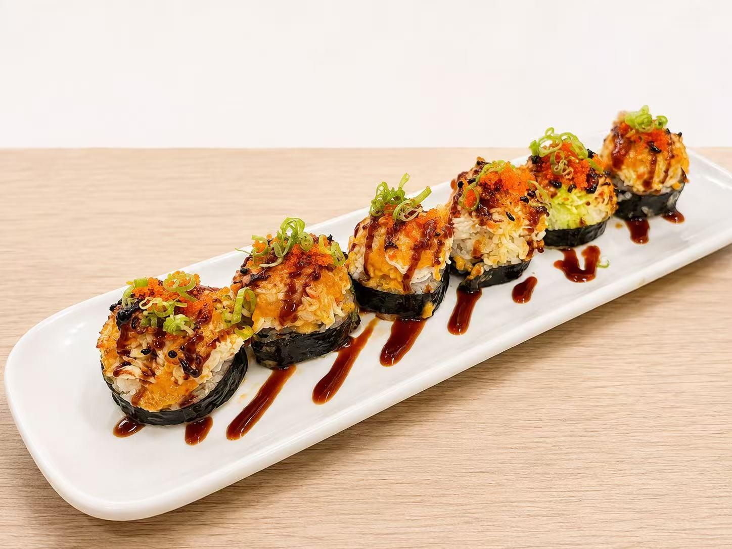 Six baked sushi rolls topped with crab, fish roe, green onion and dark sauce