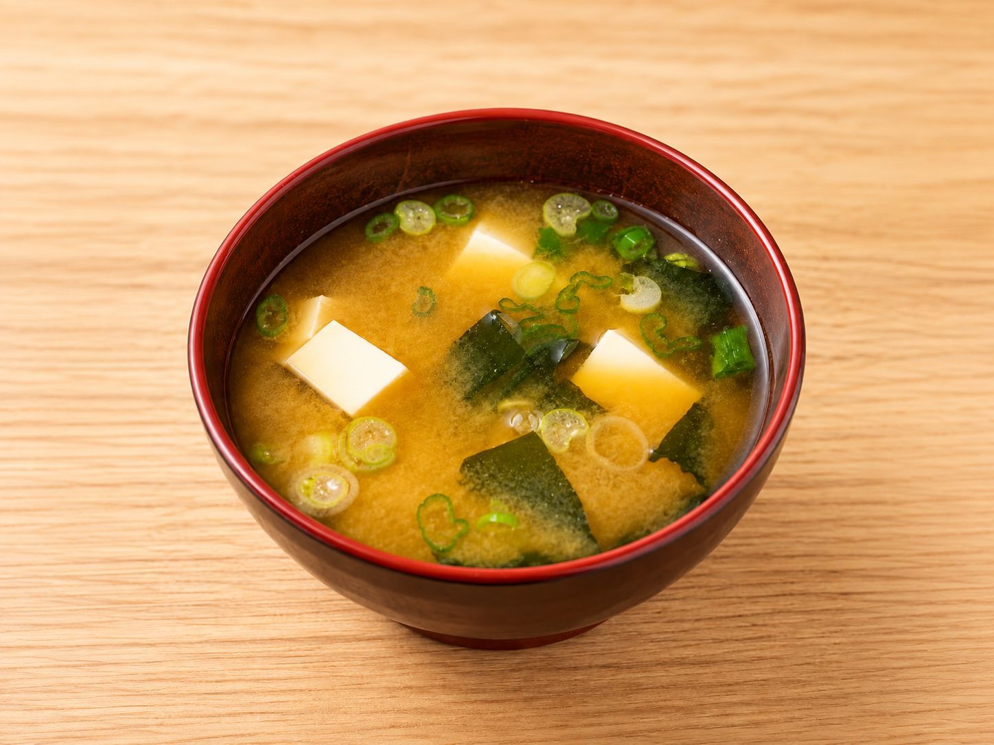 Miso soup with soft tofu, seaweed and sliced green onion in a red-rimmed bowl