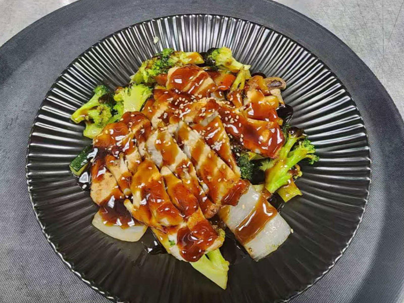 Sliced teriyaki chicken served with mixed vegetables on a black ridged plate at New Asian & Sushi Bistro, a Asian Restaurant in Elkton