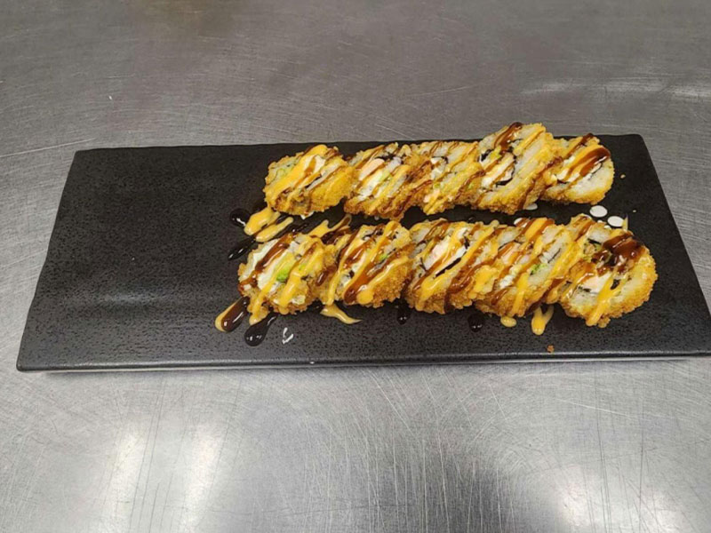 Sliced crispy sushi roll drizzled with spicy mayo and eel sauce on black plate at New Asian & Sushi Bistro, a Asian Restaurant in Elkton