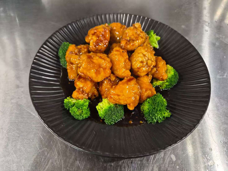 Glazed orange chicken with broccoli on textured black round plate at New Asian & Sushi Bistro, a Asian Restaurant in Elkton