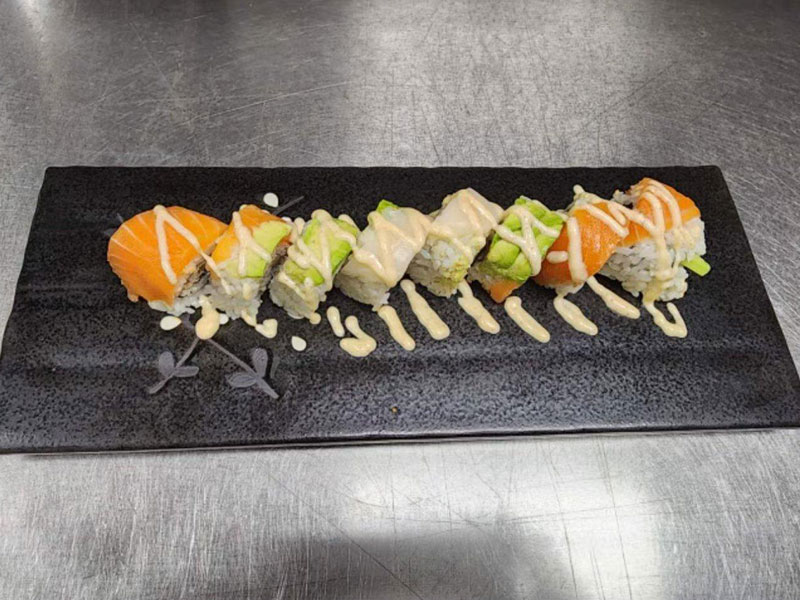 Rainbow sushi roll topped with salmon, avocado and creamy sauce on black plate at New Asian & Sushi Bistro, a Asian Restaurant in Elkton