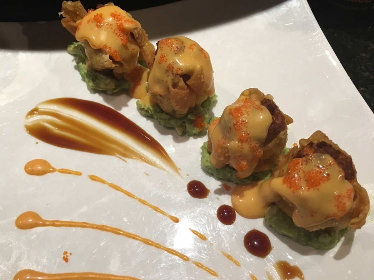 Four fried sushi bites on fresh avocado puree decorated with artistic sauce drizzles at Sakura house, a Japanese Restaurant in Willow Grove