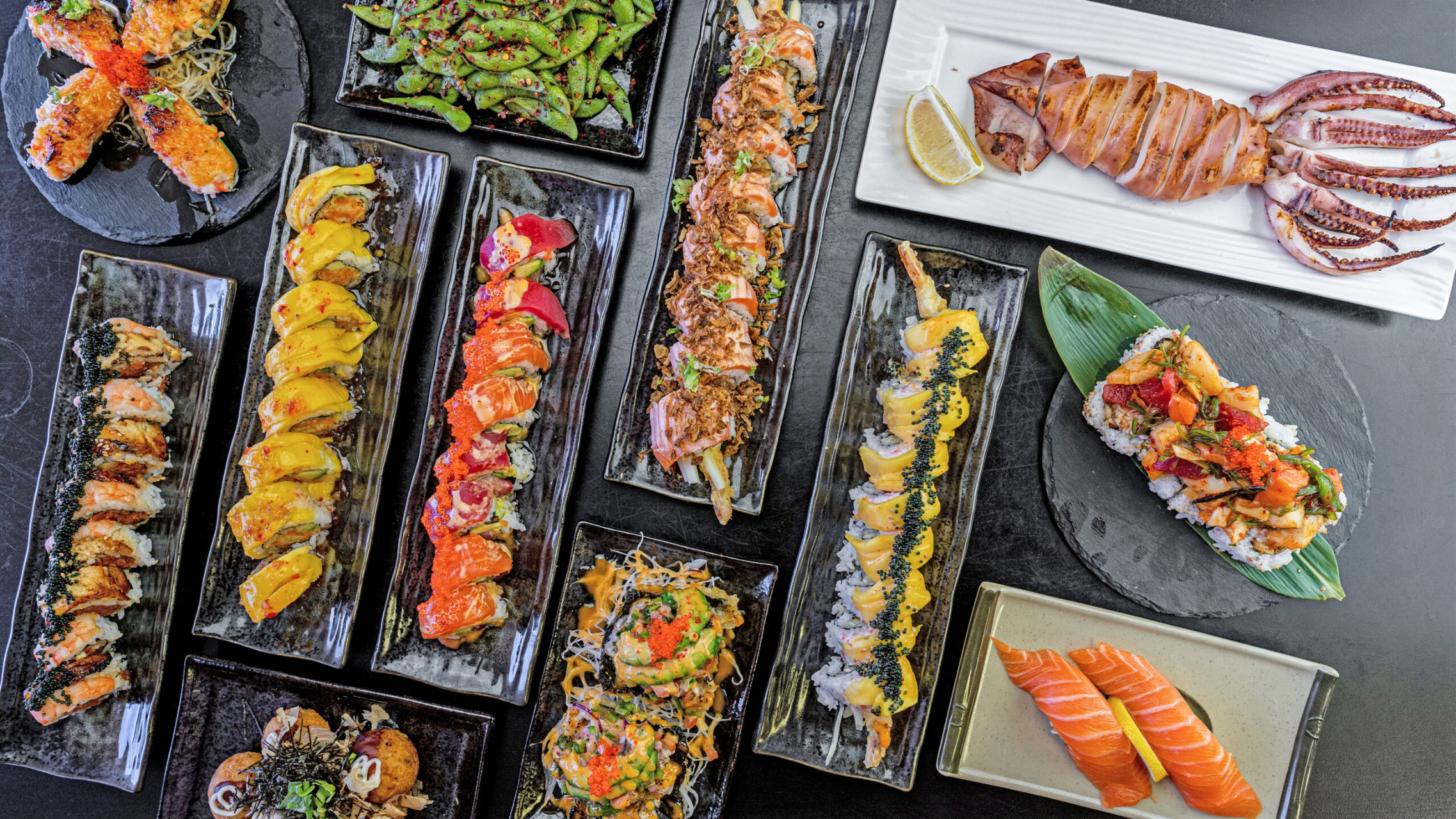 A variety of Japanese sushi rolls and seafood dishes, including salmon, edamame, and grilled squid, neatly arranged on plates at Sushi Island，a Japanese Restaurant in San Jose