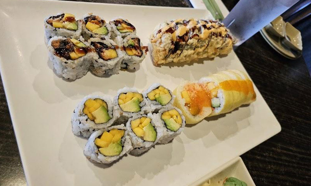 White rectangular plate with assorted mango avocado sushi rolls and tempura maki drizzled with savory sauces at Sushi & king seafood , a Sushi Restaurant in Commack