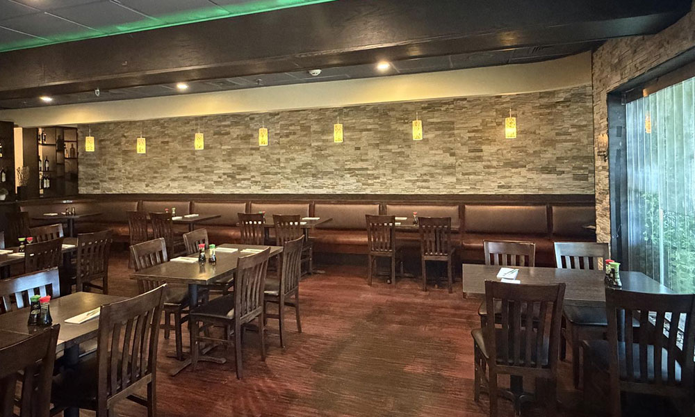 Spacious restaurant dining room with dark wooden tables, leather booths, stone accent wall and pendant lighting at Sushi & king seafood , a Sushi Restaurant in Commack
