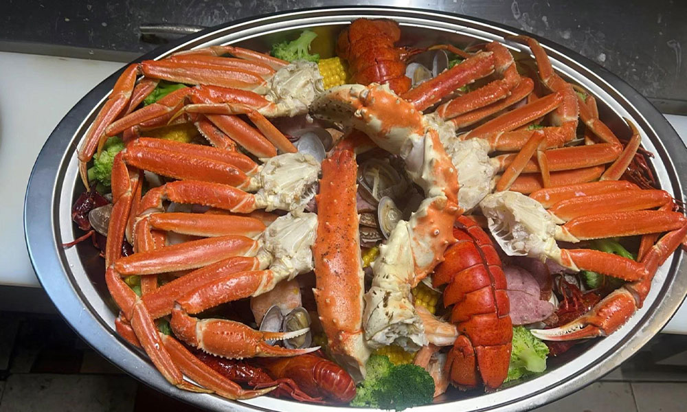 Large metal seafood boil platter piled with king crab legs, lobster tails, clams, corn and broccoli at Sushi & king seafood , a Sushi Restaurant in Commack