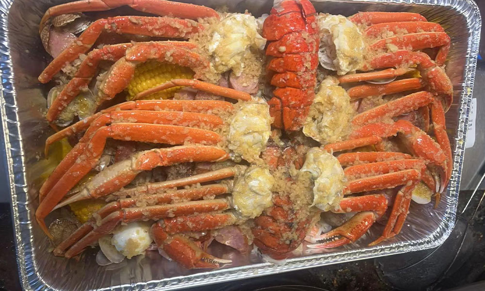 Aluminum tray loaded with seasoned snow crab legs, lobster, clams, corn and garlic butter sauce at Sushi & king seafood , a Sushi Restaurant in Commack
