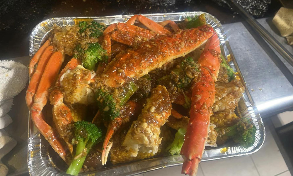 Foil tray filled with garlic butter king crab legs, broccoli and corn coated in savory spiced sauce at Sushi & king seafood , a Sushi Restaurant in Commack