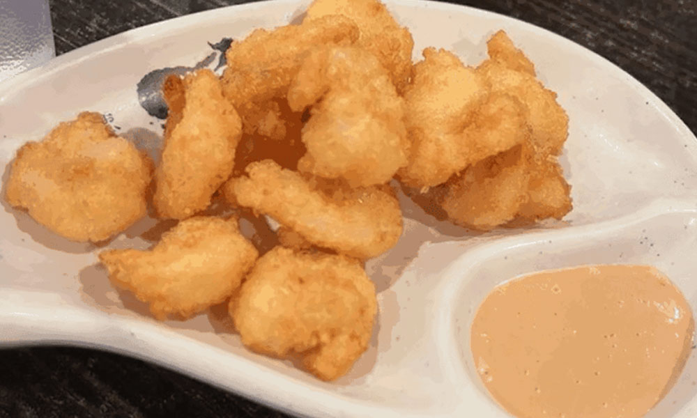 White divided ceramic plate with crispy golden fried popcorn shrimp and creamy light orange dipping sauce at Sushi & king seafood , a Sushi Restaurant in Commack