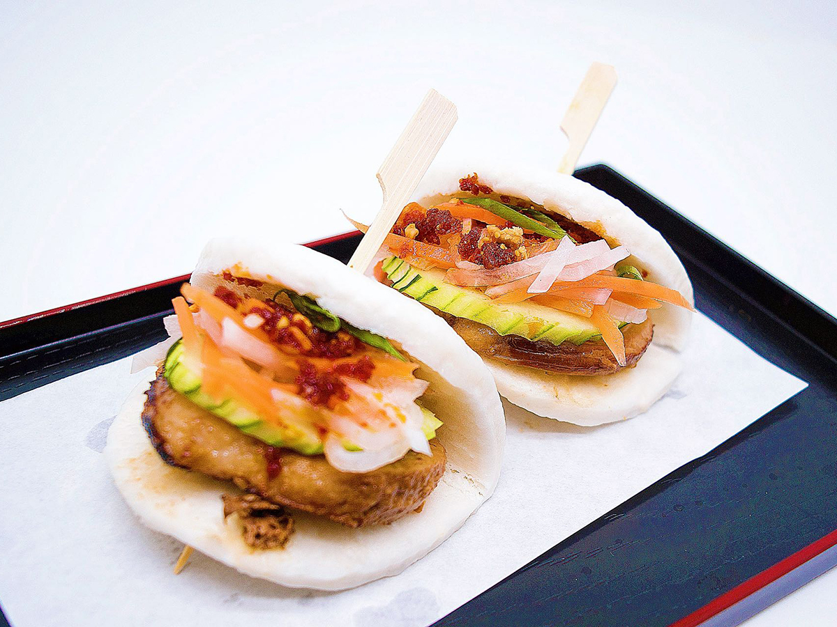 Two savory slider tacos topped with avocado, pickled veggies and chili flakes