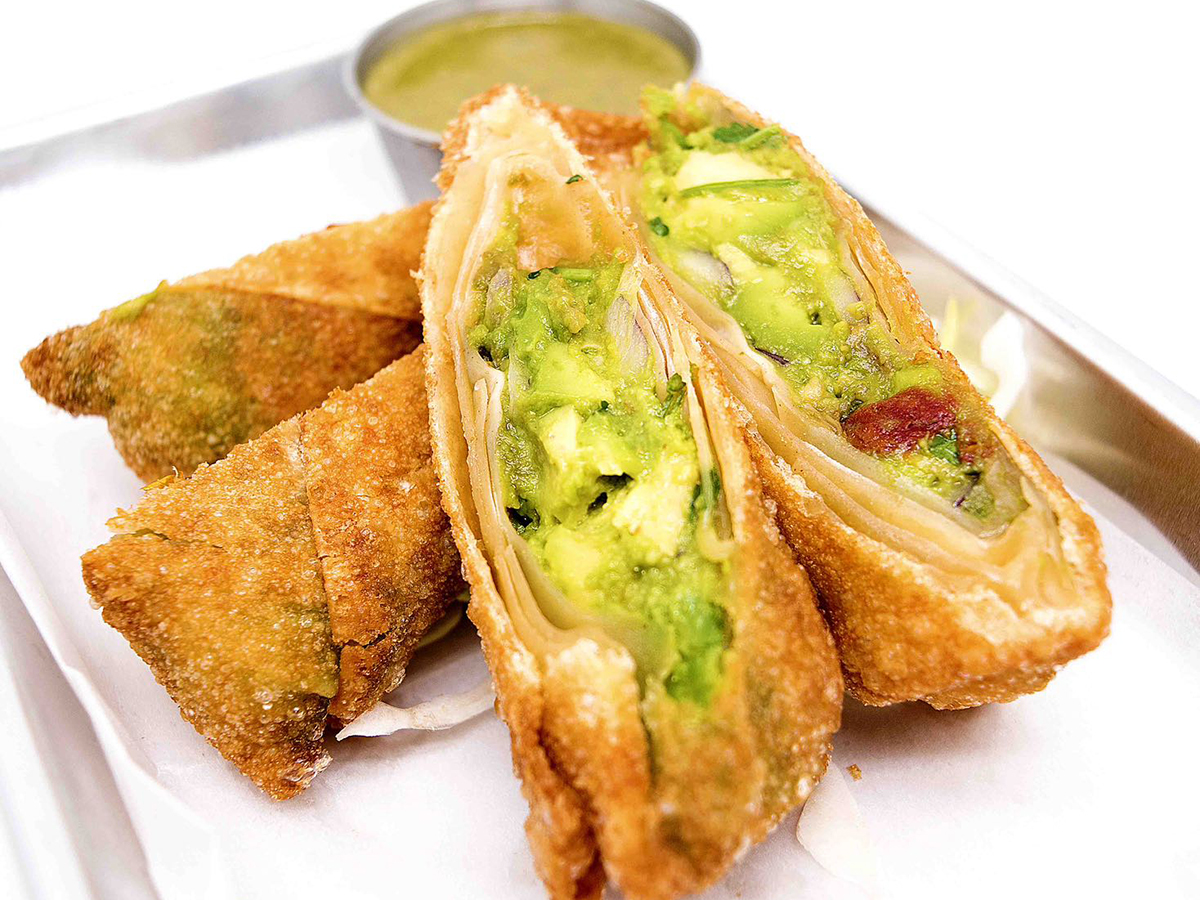 Crispy fried pastry rolls served with small metal cup of dipping sauce