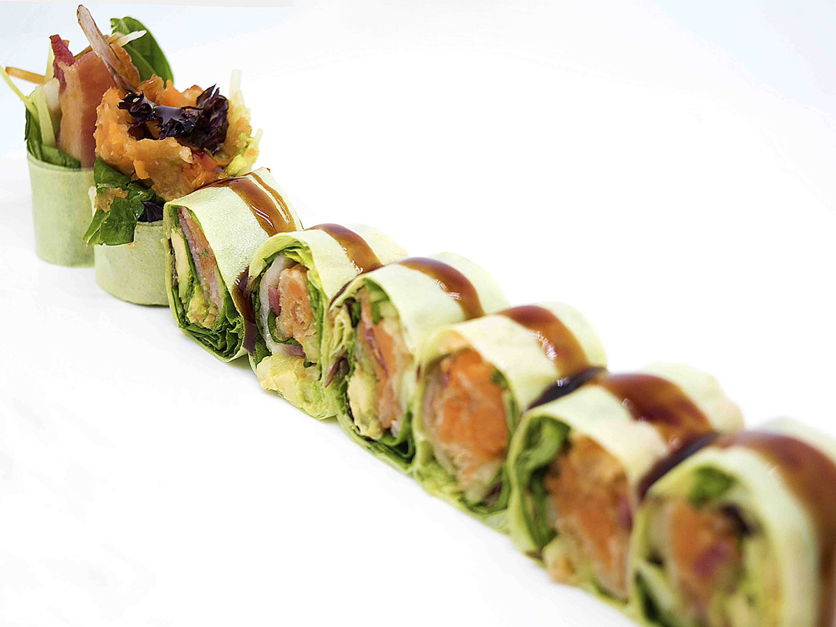 Fresh vegetable spring roll platter with sliced rolls garnished with savory sauce