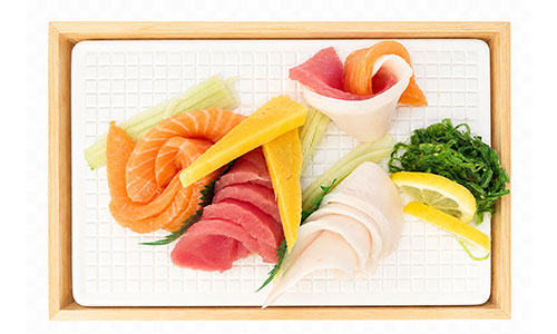 Top-down view of sashimi assortment on white grid plate inside wooden frame, garnished with tamagoyaki, seaweed salad, celery and lemon wedges.