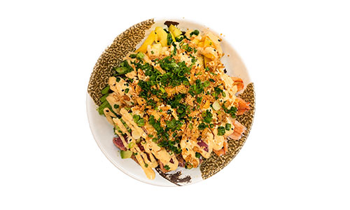 Overhead product shot of poke bowl on patterned ceramic dish, garnished with green onion, crispy shallots, sesame seeds and spicy sauce.
