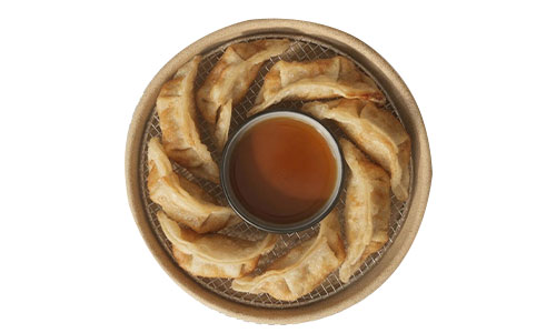 Top view of golden pan-fried gyoza arranged in bamboo steamer basket, with a small bowl of soy dipping sauce in center.
