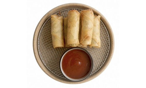 Top-down view of golden fried egg rolls on wire mesh tray, paired with small bowl of red sweet and sour sauce, plain white background.