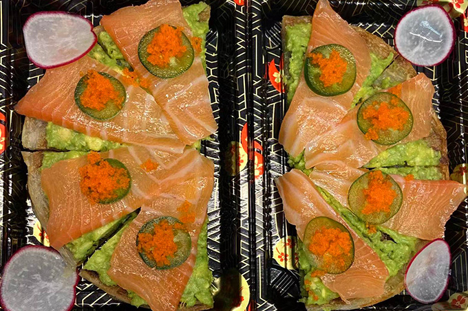 A platter of salmon sushi, garnished with toppings, in a black tray at SUSHI YA，a Japanese Restaurant in Philadelphia