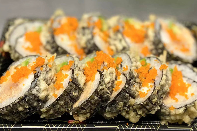 Several mixed sushi rolls, topped with orange ingredients, placed together at SUSHI YA，a Japanese Restaurant in Philadelphia