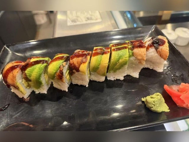 Tasty sushi roll with avocado, unagi (eel) and rice, drizzled with sauce, served with wasabi and