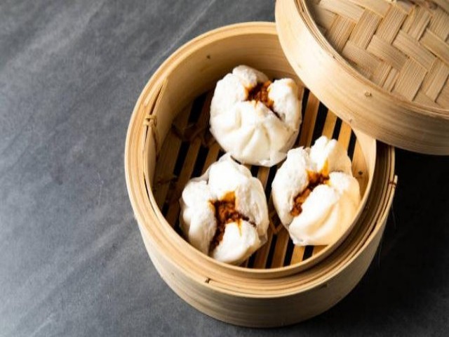 Three fluffy steamed buns filled with barbecued pork, served in a bamboo steamer.