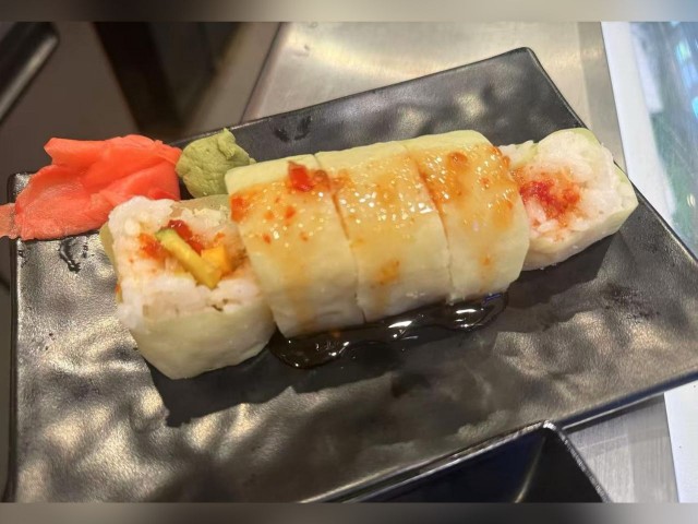 Unique sushi roll with various fillings and rice, topped with sauce, served with wasabi and pickled ginger.
