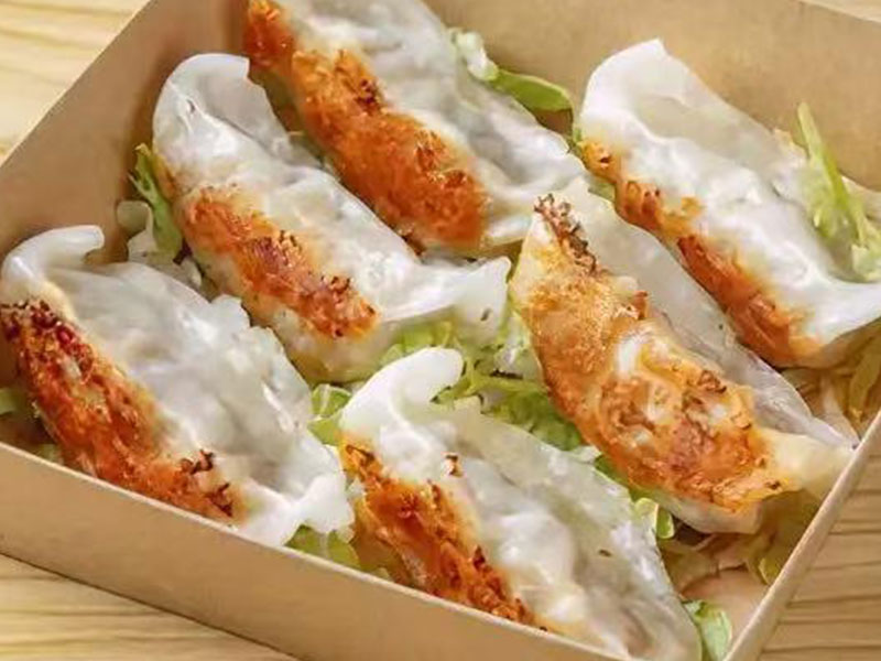 Brown paper takeout box holding six crispy pan-fried gyoza dumplings over fresh lettuce at Takuma Hibachi , a Japanese Restaurant in Hillsboro