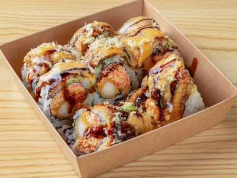 Brown paper takeout box filled with loaded specialty sushi rolls drizzled with creamy and eel sauces at Takuma Hibachi , a Japanese Restaurant in Hillsboro