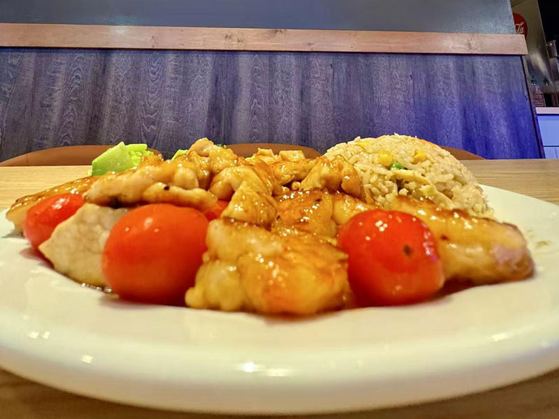 White ceramic dinner plate with glazed stir-fried fish, cherry tomatoes and a scoop of house fried rice at Takuma Hibachi , a Japanese Restaurant in Hillsboro