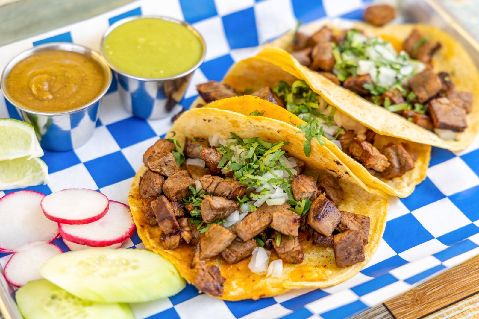 Carne asada tacos topped with diced onions and cilantro, served with salsa, radishes, cucumber and lime Carne asada tacos topped with diced onions and cilantro, served with salsa, radishes, cucumber and lime