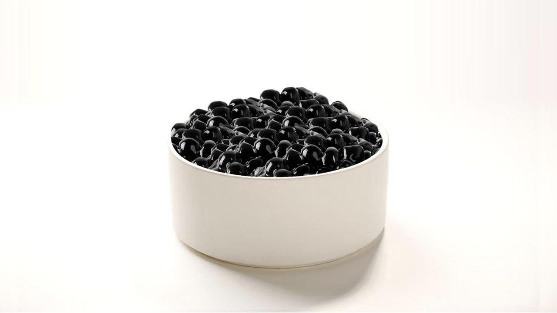 A white ceramic bowl filled to the brim with glossy, translucent black tapioca boba pearls glistening under light against a clean white backdrop at Tart Tart Bakery, a Cake shop in Hicksville