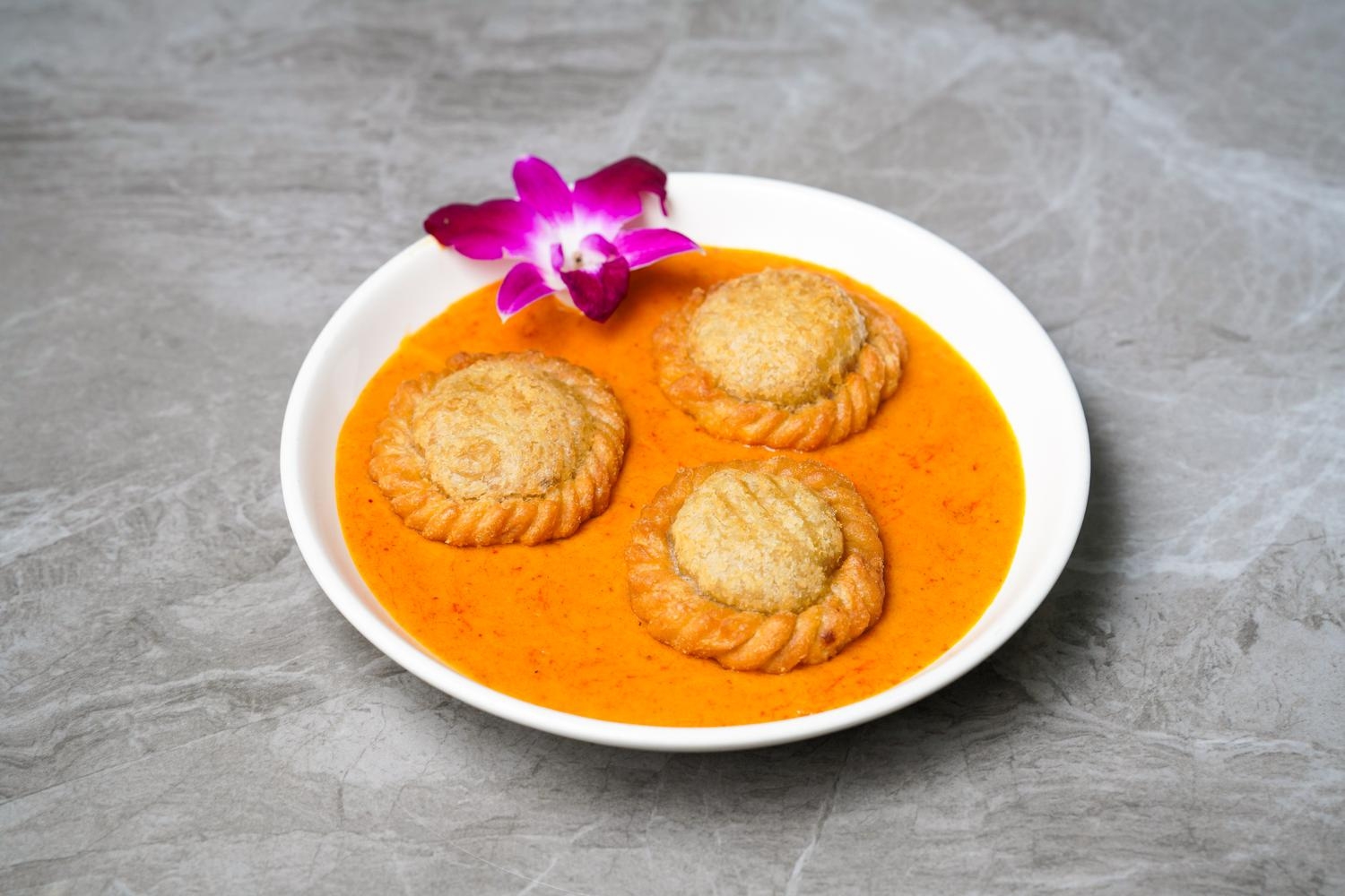 Curry sauce with three crispy stuffed pastries and orchid decoration