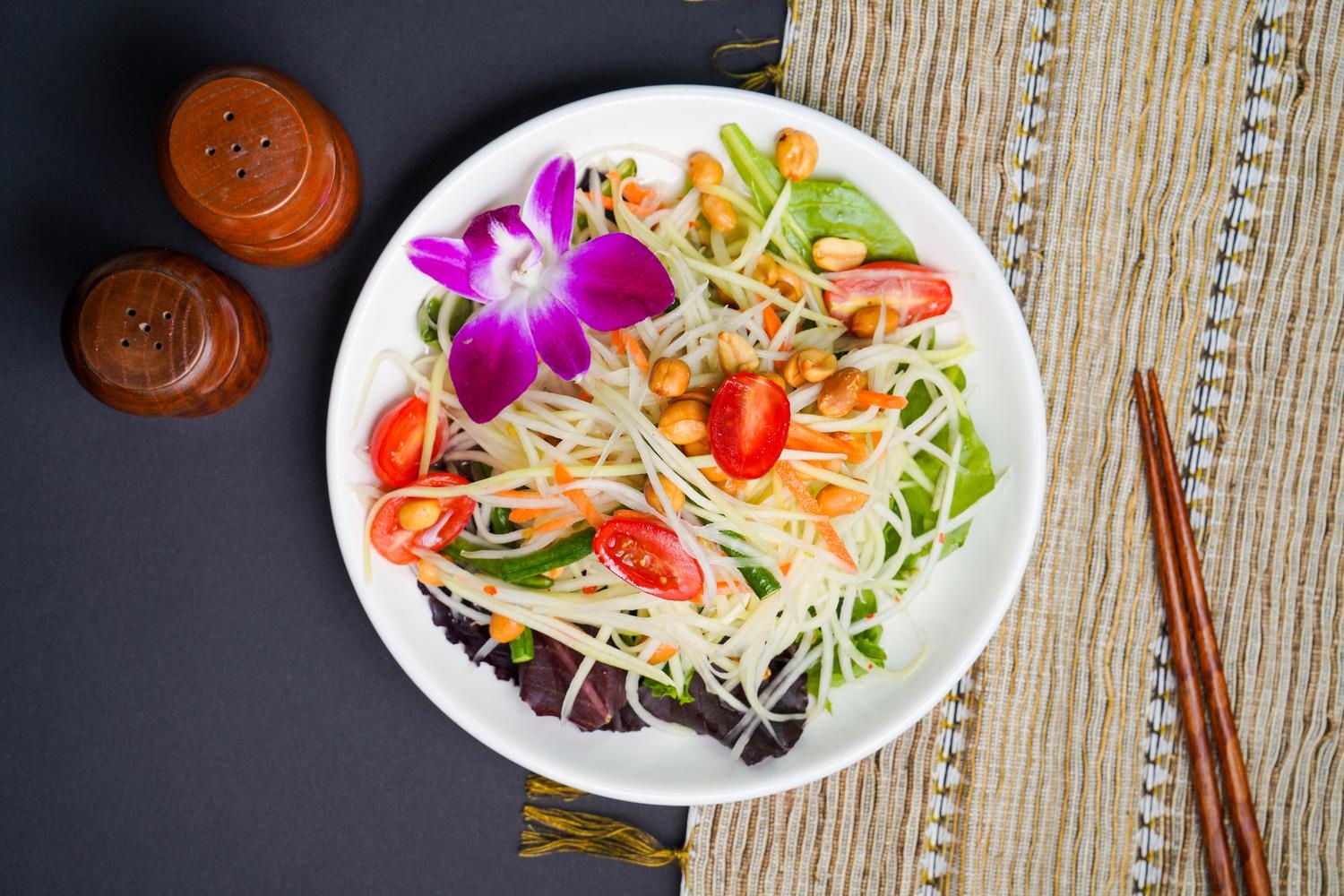 Spicy green papaya salad with tomato, peanut and orchid garnish