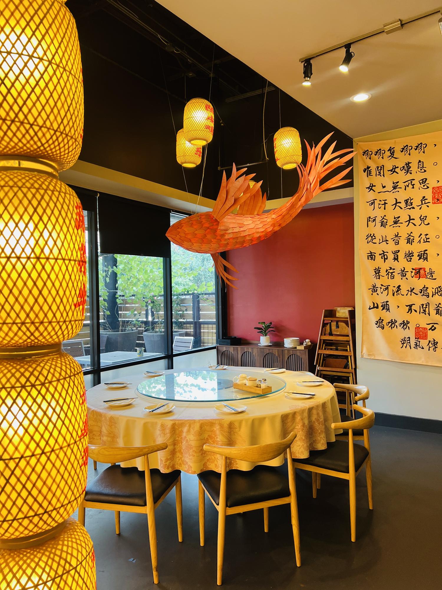Elegant dining room with round table, yellow tablecloth, lanterns, and Chinese calligraphy on the wall.