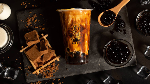 Top-down shot of brown sugar boba milk tea surrounded by raw brown sugar and tapioca pearls at Tiger Sugar, a Bubble tea store in Philadelphia