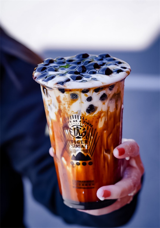 Hand gripping signature brown sugar latte bubble tea with thick tapioca pearls on top at Tiger Sugar, a Bubble tea store in Philadelphia