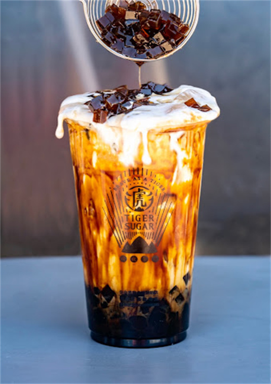 Bubble tea cup topped with whipped cream as coffee jelly is poured from a strainer above at Tiger Sugar, a Bubble tea store in Philadelphia