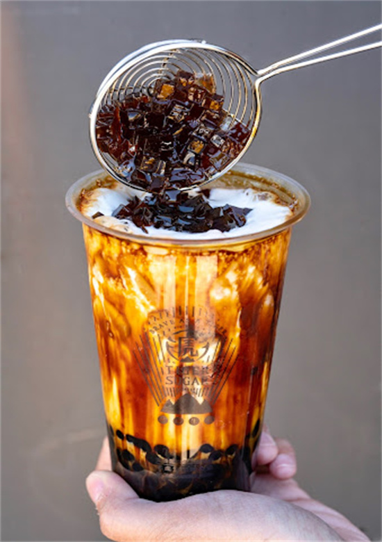 Hand holding bubble tea while coffee jelly toppings are added from a metal strainer at Tiger Sugar, a Bubble tea store in Philadelphia