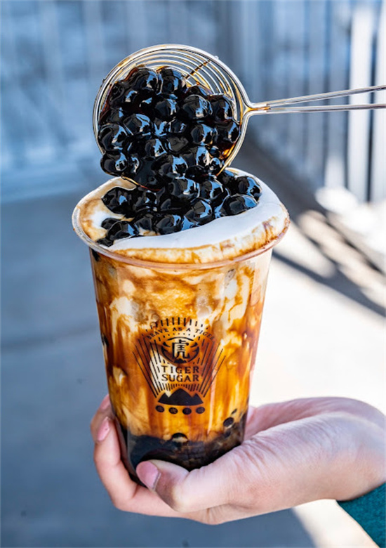 Metal strainer pouring black tapioca pearls onto tiger stripe bubble tea cup held in hand at Tiger Sugar, a Bubble tea store in Philadelphia