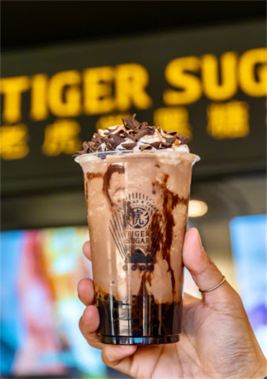 Hand holding chocolate bubble tea with whipped cream and chocolate shavings topping at Tiger Sugar, a Bubble tea store in Philadelphia