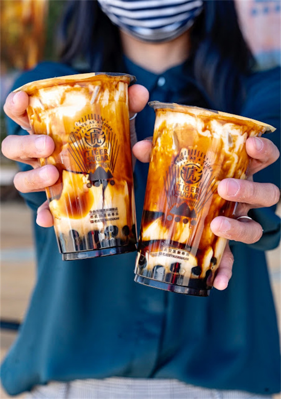Person holding two tiger sugar brown sugar boba milk tea cups at Tiger Sugar, a Bubble tea store in Philadelphia